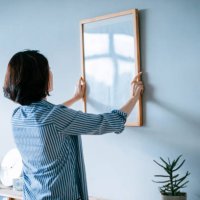 young asian woman decorating and putting up a picture frame on the wall at home - home decoration stock pictures, royalty-free photos & images