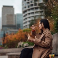young asian woman eating takeaway lunch while sitting on the bench in city park - junk food stock pictures, royalty-free photos & images