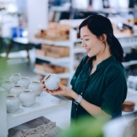 young asian woman shopping for household necessities in a homeware store looking at a ceramic plant pot - home decoration stockfoto's en -beelden