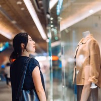 young asian woman standing outside a boutique looking at window display while shopping in shopping mall. window shopping. sale season - fashion stock pictures, royalty-free photos & images