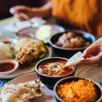 young asian woman tasting authentic classic indian food with assorted dishes freshly served on the table in restaurant. close-up of her hand dipping naan bread on the butter chicken. tourist exploring local cuisines when trav