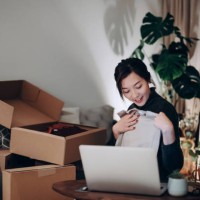 young asian woman unboxing new purchase clothings from cardboard box that received from her online shopping retail delivery at home. she is happy and excited to see the content from the box. online shopping, trustworthy parce