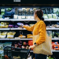 young asian woman with shopping cart, carrying a reusable shopping bag, shopping for fresh organic fruits and vegetables in supermarket. environmentally friendly concept. zero waste and plastic free. eco friendly shopping. su
