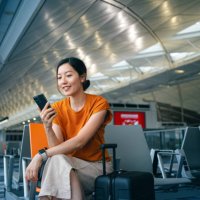 young asian woman with suitcase using smartphone while waiting for her flight at airport terminal. asian businesswoman on business travel. lifestyle and technology. travel and vacation concept - travel stock pictures, royalty