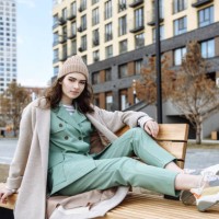 young beautiful teenage girl in a hat and coat sits on a bench and poses against the background of a city street - fashion stock pictures, royalty-free photos & images