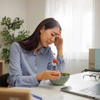 young beautiful woman experiencing headache while having breakfast at home office - food stock pictures, royalty-free photos & images