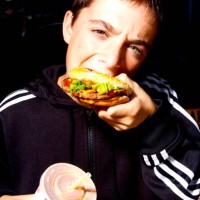 Young boy eating a fast food burger and holding a drink.