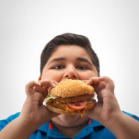 young boy eating a large burger in hand. (obesity) - junk food stock pictures, royalty-free photos & images