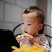 young boy eating and playing digital tablet in cafe - junk food stock pictures, royalty-free photos & images