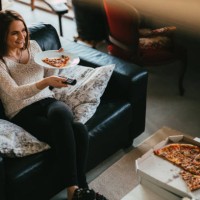 young casually dressed woman eating pizza in front of a tv - junk food stock pictures, royalty-free photos & images