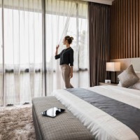 young caucasian woman at home, looking out of modern bedroom window - home decoration stockfoto's en -beelden