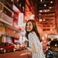 young cheerful asian woman looking back in front of the neon lights of hong kong on the streets at night while holding her camera - travel stock pictures, royalty-free photos & images