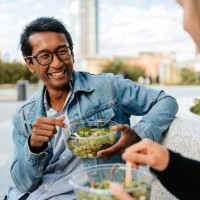 young couple eating a salad and talking on the bench in milan - junk food stock pictures, royalty-free photos & images