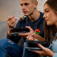 young couple enjoying healthy takeaway lunch and watching a movie on laptop - junk food stock pictures, royalty-free photos & images