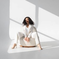 young female stylist with dark wavy hair wearing white suit sitting in bright empty room - fashion stock pictures, royalty-free photos & images