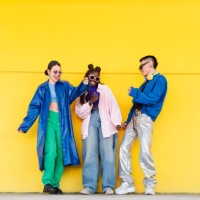 young friends dancing energetically, wearing trendy outfits against bright yellow backdrop, expressing vibrant youthful style - fashion stock pictures, royalty-free photos & images