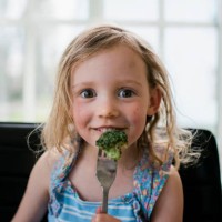 young girl eating broccoli at home with a messy face - food stock pictures, royalty-free photos & images