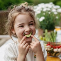 young girl eating slice of cucumber, having fun, waiting for grilled food. family barbecue in backyard, spending quality time outdoors together. - food stock pictures, royalty-free photos & images