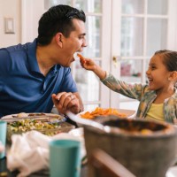 young girl feeding her father at dinner table - food stock pictures, royalty-free photos & images