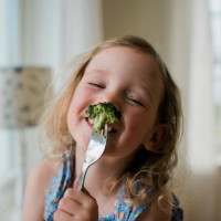 young girl laughing with a messy face whilst eating broccoli - food stock pictures, royalty-free photos & images