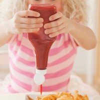 young girl squeezing ketchup on french fries - junk food stockfoto's en -beelden
