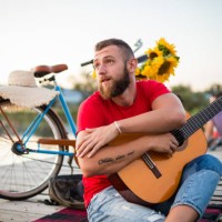 young hipster guy holding acoustic guitar while sitting on dock in nature. summer and travel concept. - concert stock pictures, royalty-free photos & images