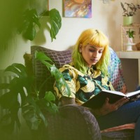 young hipster woman reading a book in her living room - home decoration photos et images de collection