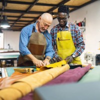 young man black ethnicity, learning craft from an senior tailor, at the leather workshop - fashion stock pictures, royalty-free photos & images
