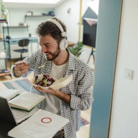 young man eating take away meal and looking at the laptop - junk food stock pictures, royalty-free photos & images