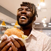young man enjoying having burger at a restaurant - junk food stock pictures, royalty-free photos & images