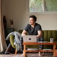 young man in pajamas smiling while working on a laptop at home - home decoration stock pictures, royalty-free photos & images