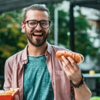 young man is eating hot dog on the street - junk food stock pictures, royalty-free photos & images