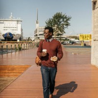 young man with coffee cup and hamburger walking at the harbour - junk food stock pictures, royalty-free photos & images