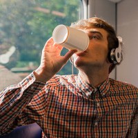 young man with headphones drinking coffee to go in a train - junk food stock pictures, royalty-free photos & images