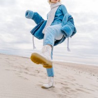 young modern blond woman in warm jeans outfit and a scarf posing on a sandy beach. sea background - fashion stock pictures, royalty-free photos & images