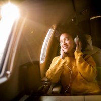 young modern woman sitting in a private jet, listening to music through the headphones and looking through the window - travel stock pictures, royalty-free photos & images