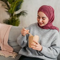 young muslim woman eating take out food on the sofa at home - junk food stock pictures, royalty-free photos & images