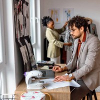 young tailor using laptop for work in his workshop. - fashion stock pictures, royalty-free photos & images