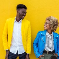 young trendy black multiracial friends looking each other over yellow background. african man and latin american woman standing together outdoors. - fashion fotografías e imágenes de stock