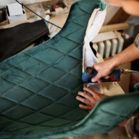 young upholstery worker applying fabric on a chair with a pneumatic stapler in the workshop - home decoration stockfoto's en -beelden