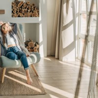 young woman at home sitting on modern chair in front of window relaxing in her living room reading book and drinking coffee or tea - home decoration stock pictures, royalty-free photos & images