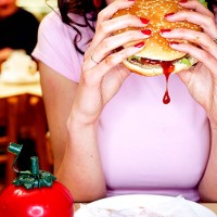 young woman biting into hamburger in diner - junk food stockfoto's en -beelden
