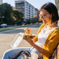 young woman eating a salad on a bench in the park - junk food stock pictures, royalty-free photos & images