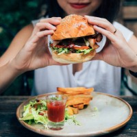 young woman eating burger at restaurant with outdoor seating - junk food stock pictures, royalty-free photos & images