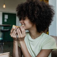 young woman eating slice pizza in the living room at home - junk food stock pictures, royalty-free photos & images