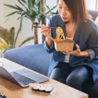 young woman eating takeaway food while using laptop - junk food stock pictures, royalty-free photos & images