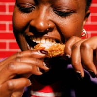 young woman enjoying chicken wings in front of red brick wall - junk food stock pictures, royalty-free photos & images