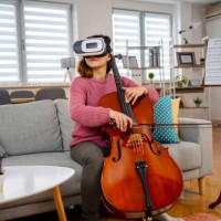 young woman experiencing virtual reality of a sold out concert while playing violoncello at home - concert stockfoto's en -beelden