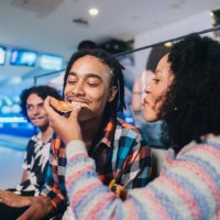 young woman giving pizza to her friend at a bowling club - food stockfoto's en -beelden