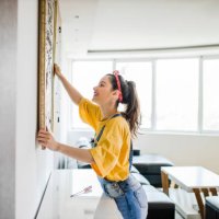 young woman hanging a picture on a wall with a look of concentration - home decoration stock pictures, royalty-free photos & images